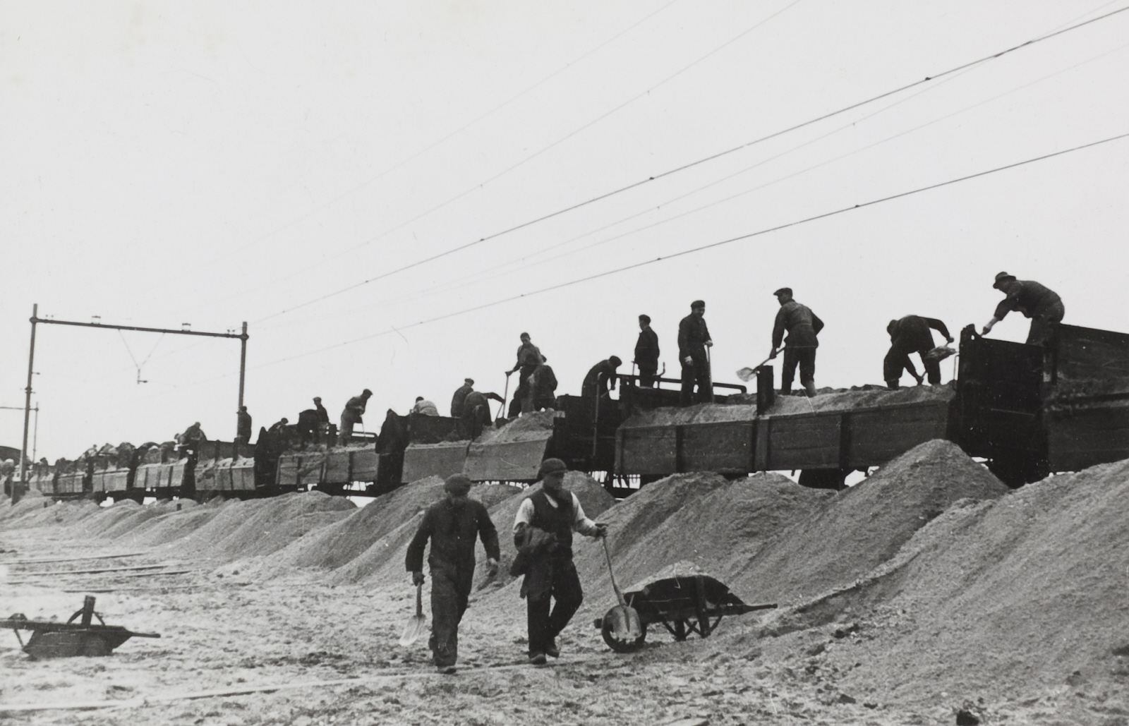 Werkmannen scheppen zand van wagens bij Duivendrecht